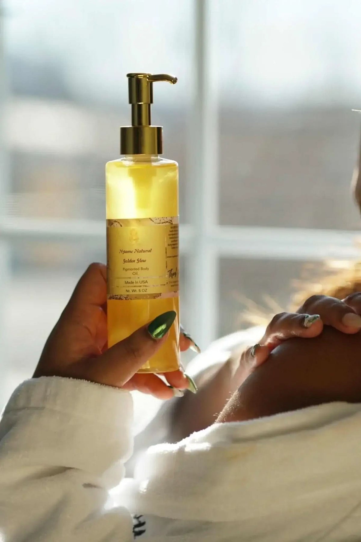 RoyalLuxsLLC 24k gold body oil in a clear pump bottle held by a person applying it to their shoulder