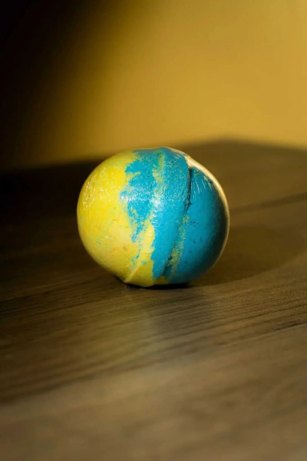 RoyalLuxsLLC luxurious herbal bath bomb in yellow and blue on wooden surface with warm lighting