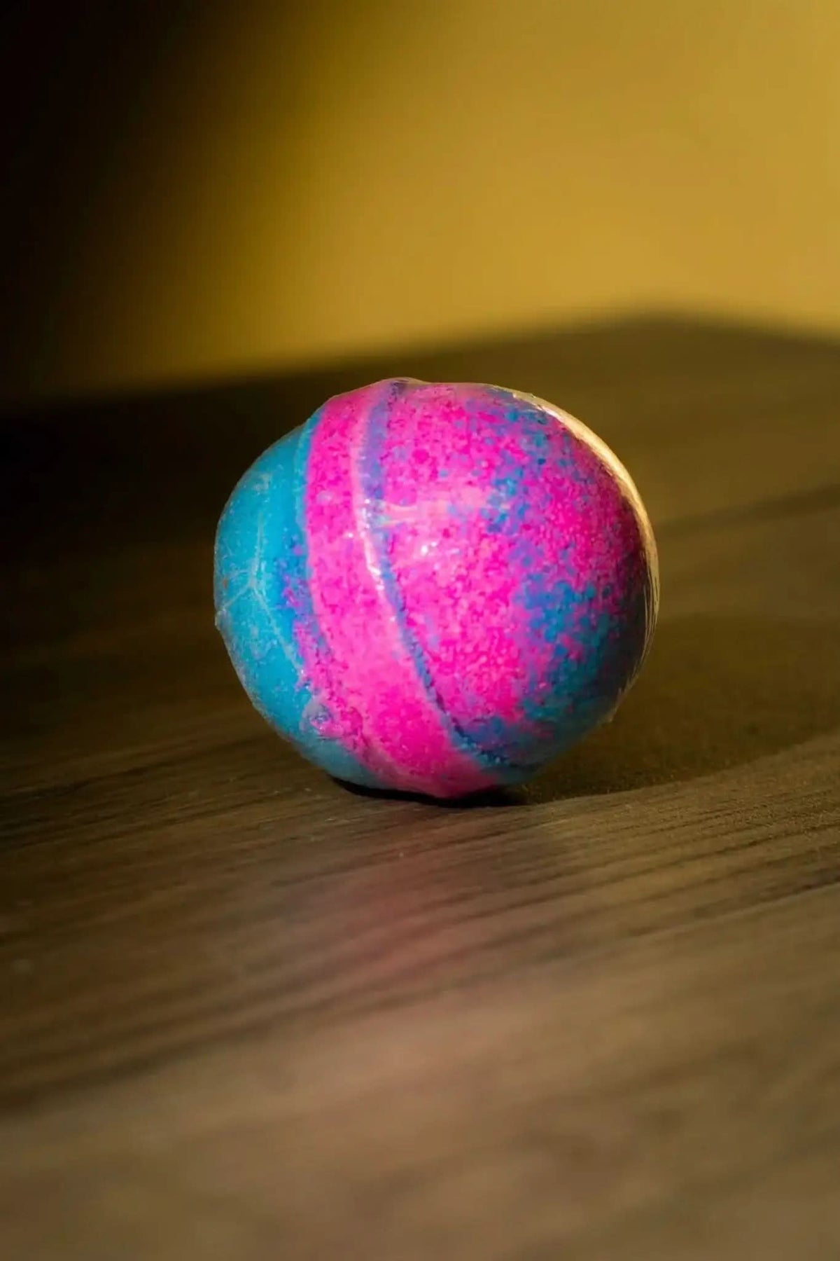 RoyalLuxsLLC luxurious herbal bath bomb in vibrant pink and blue colors on wooden surface