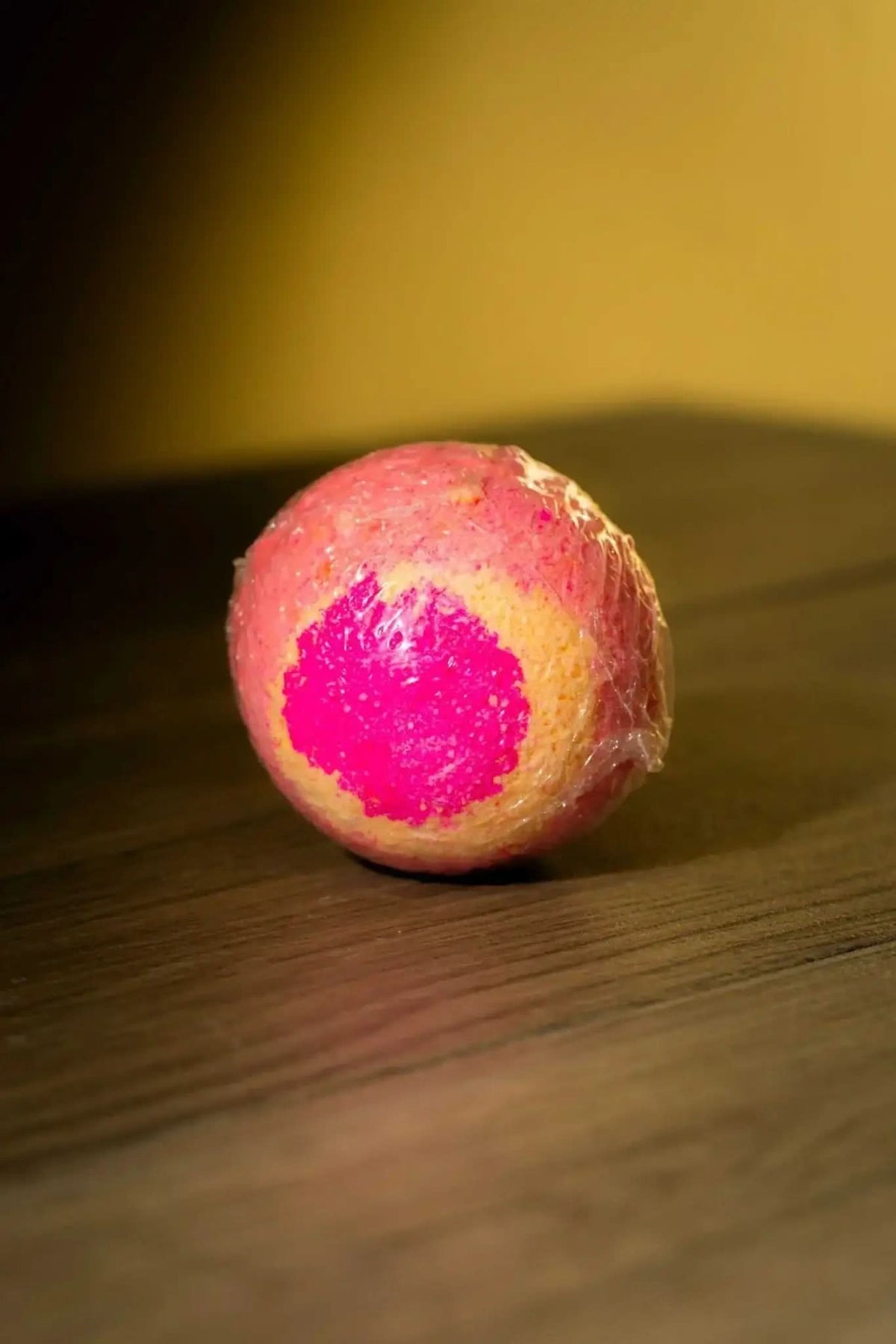 RoyalLuxsLLC luxurious herbal bath bomb wrapped, round pink and orange color on wooden surface