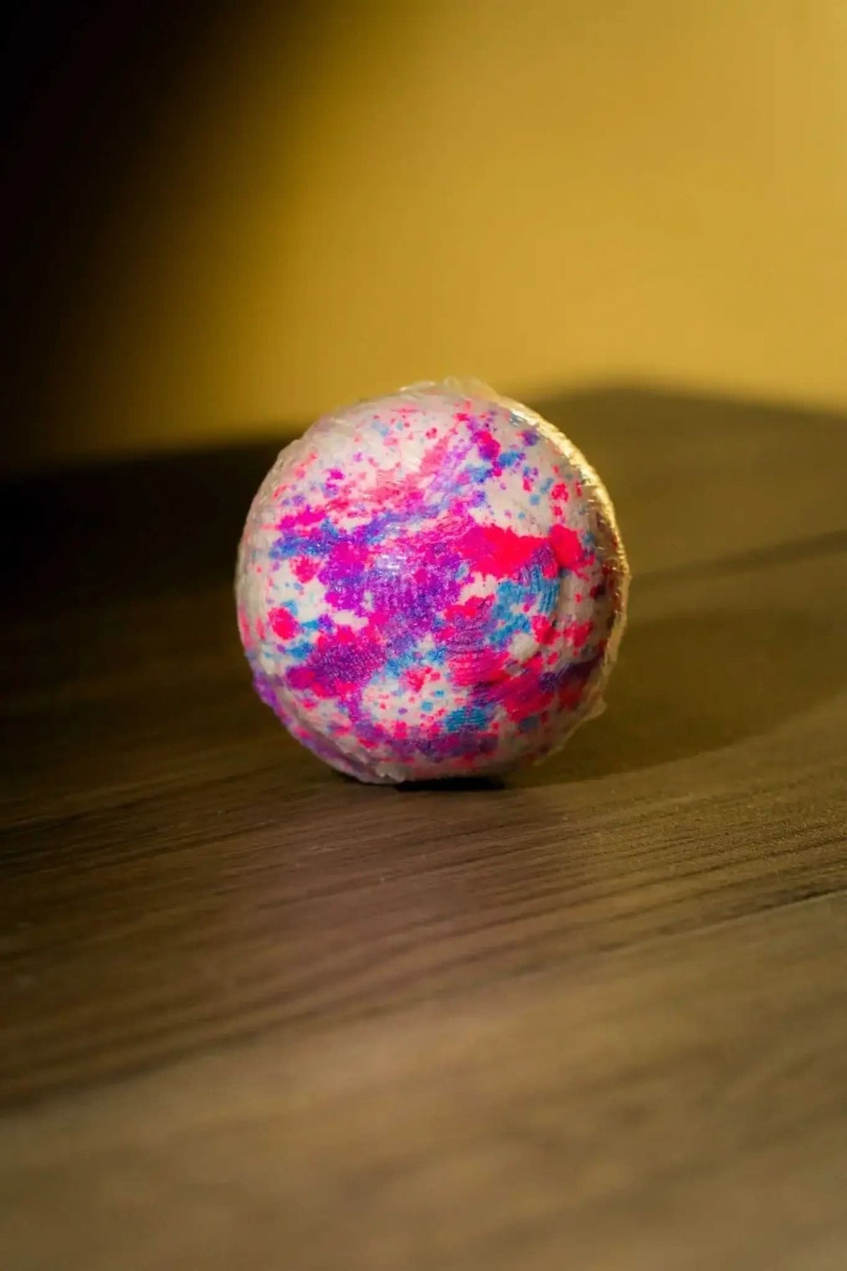 RoyalLuxsLLC luxurious herbal bath bomb with pink and purple speckles on wooden surface