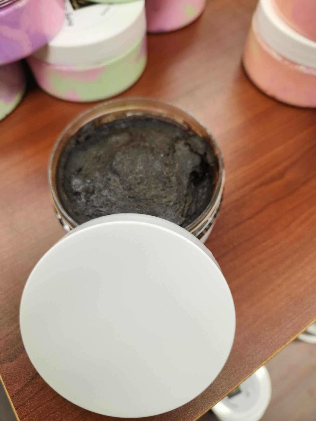 Open jar of African black soap paste by RoyalLuxsLLC on wooden surface with other skincare containers