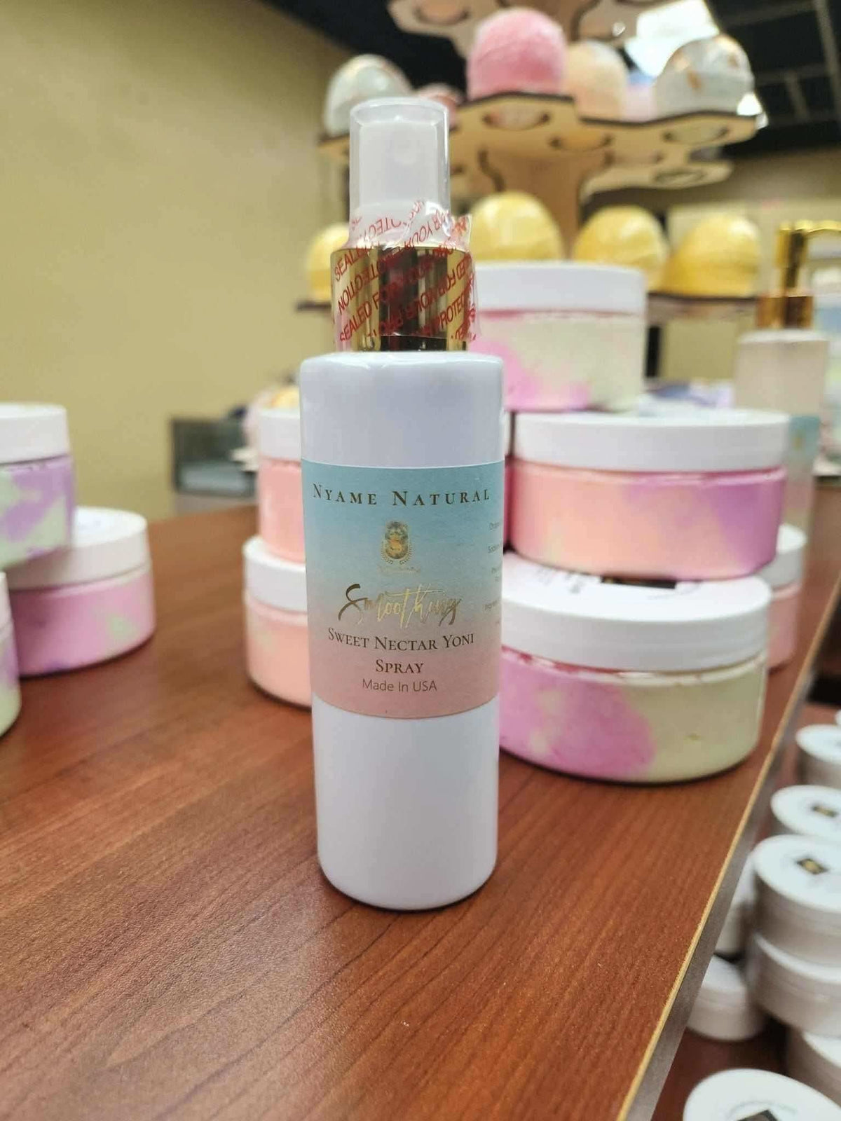 RoyalLuxsLLC natural yoni spray bottle on wooden surface with pink and white skincare containers in background