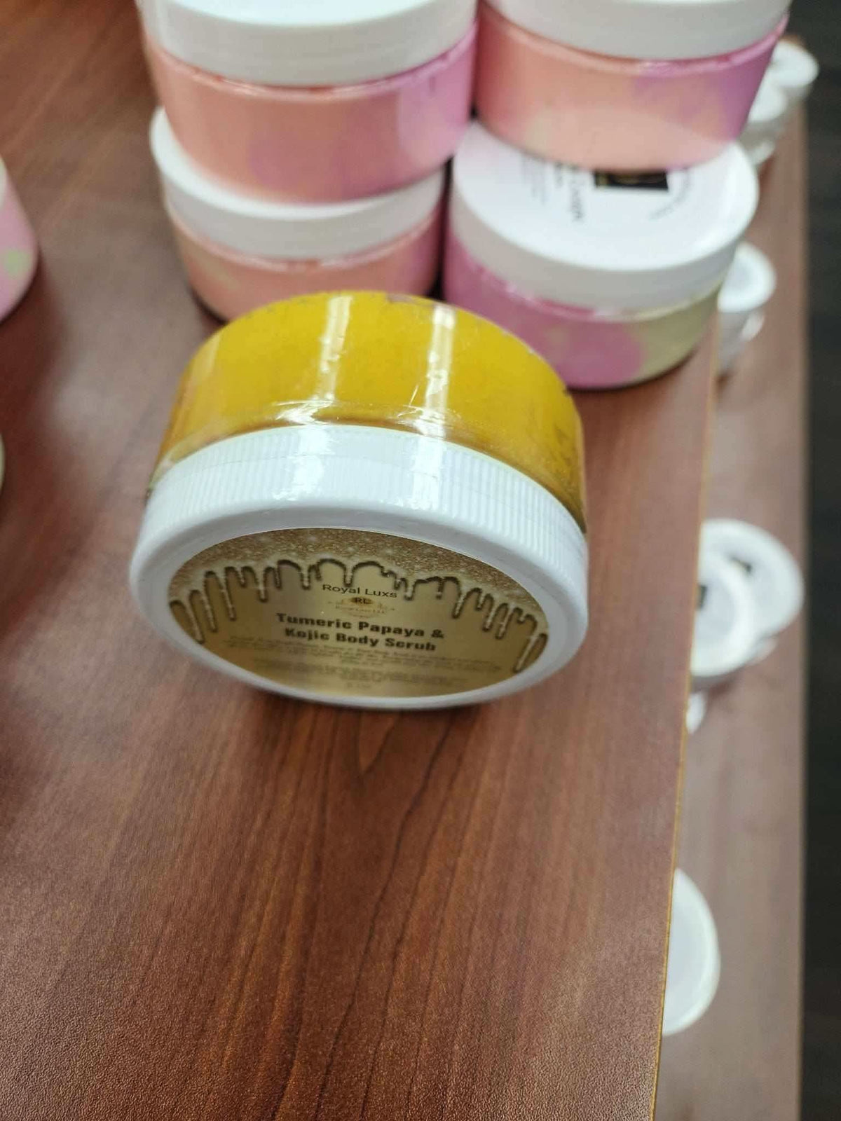 RoyalLuxsLLC turmeric papaya body scrub in a clear jar with white lid on wooden surface