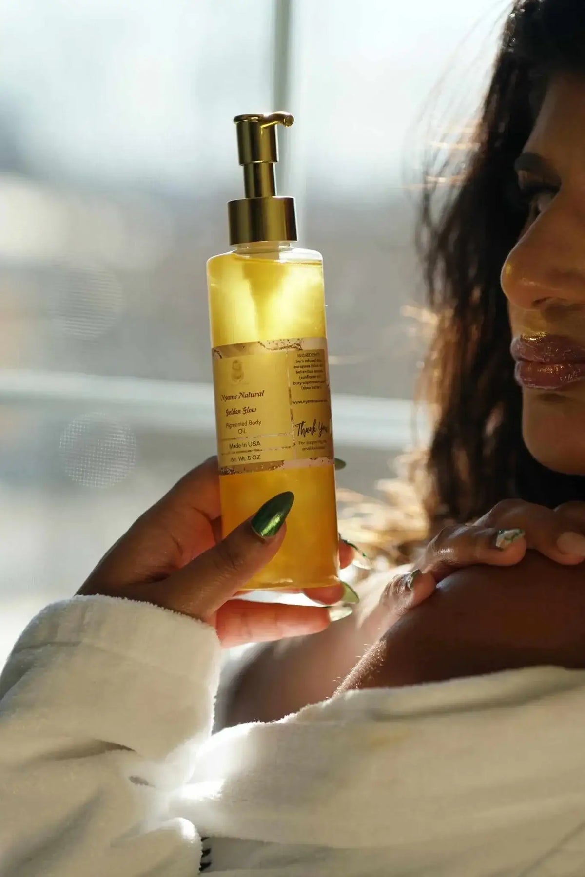 Woman holding a bottle of 24k Gold Pigmented body oil, showcasing radiant skin and luxurious moisturizing properties.
