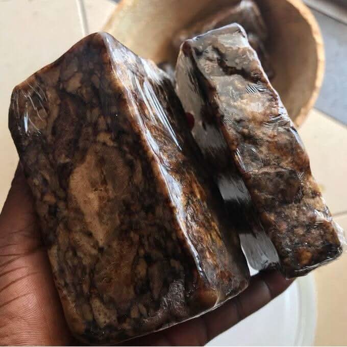 Hand holding two bars of African black soap raw unrefined with natural texture and dark marbled appearance