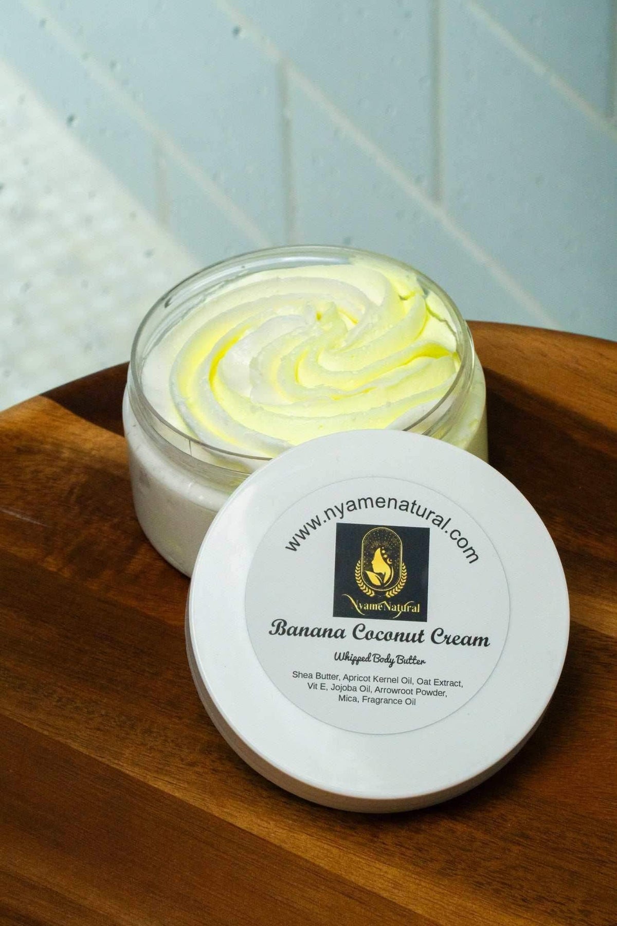 Banana Coconut cream body Butter in a glass jar on a wooden table, showcasing its creamy texture and vibrant color.