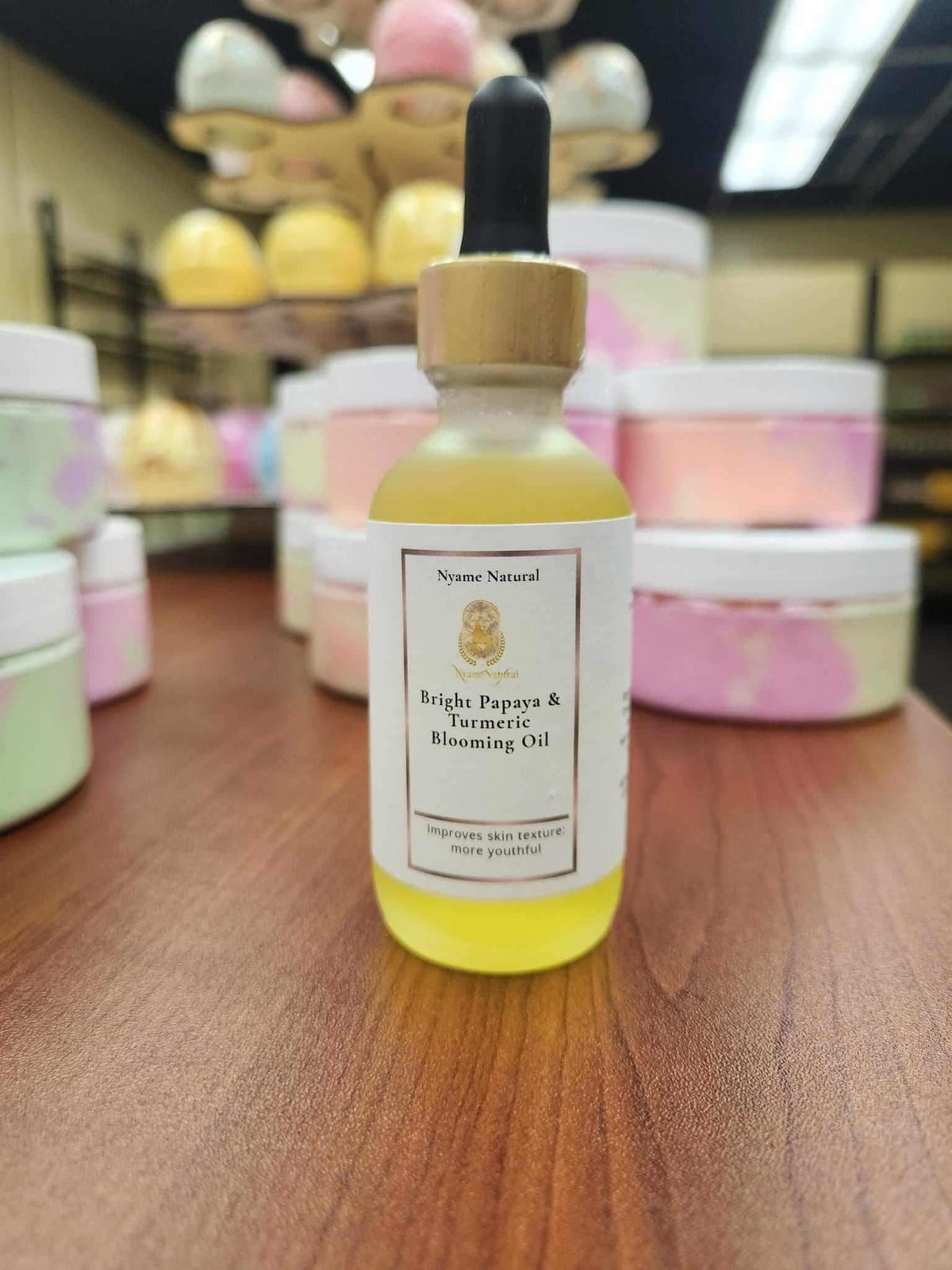 Bright Papaya & Turmeric Blooming Oil in a glass bottle on a wooden table, surrounded by colorful skincare products.