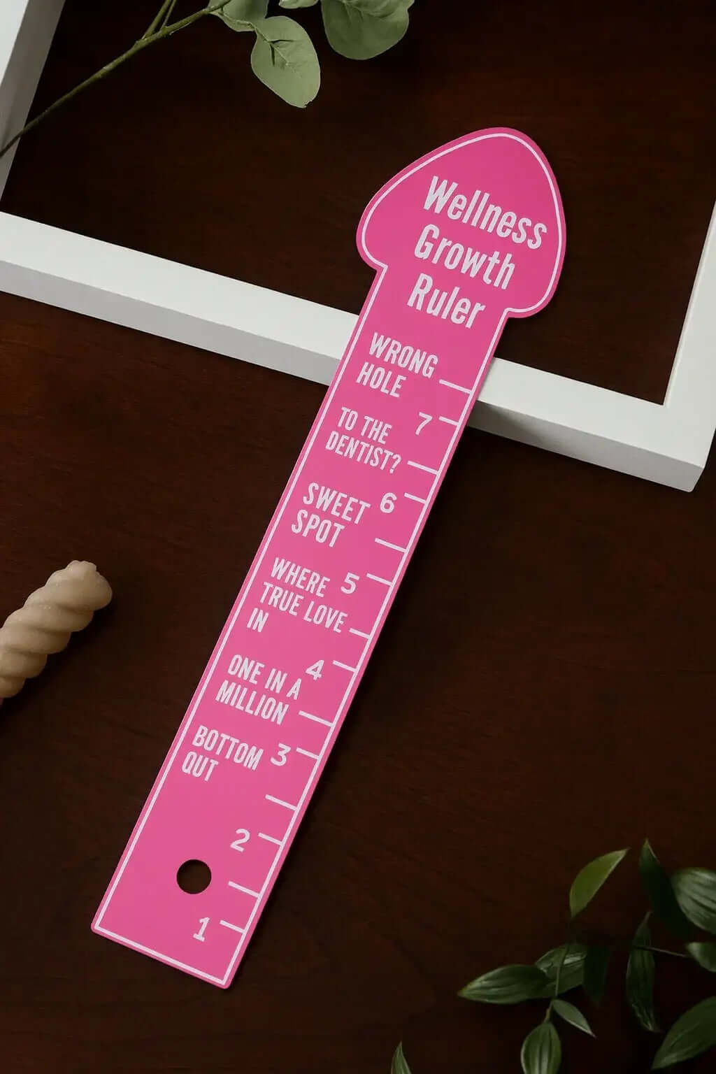 Pink eggplant ruler measurement tool with wellness growth markings from RoyalLuxsLLC on a dark wooden surface