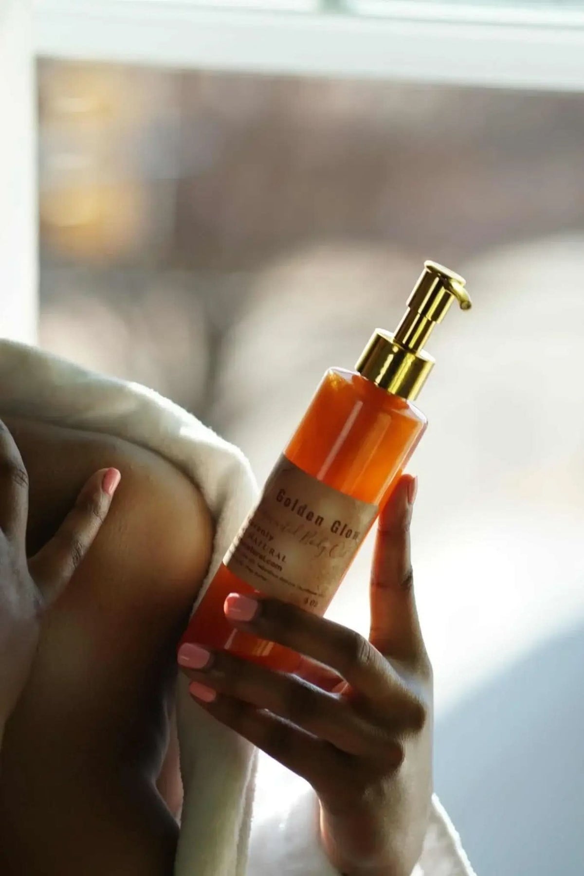 RoyalLuxsLLC copper body oil in a pump bottle held by a person with peach nail polish