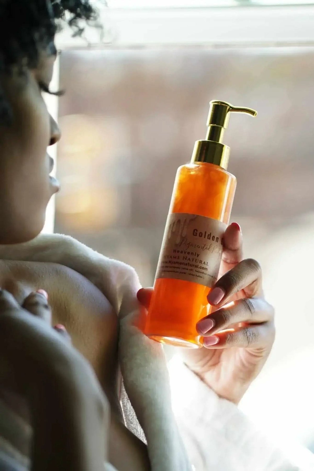 Person holding RoyalLuxsLLC copper body oil in an amber pump bottle near window light