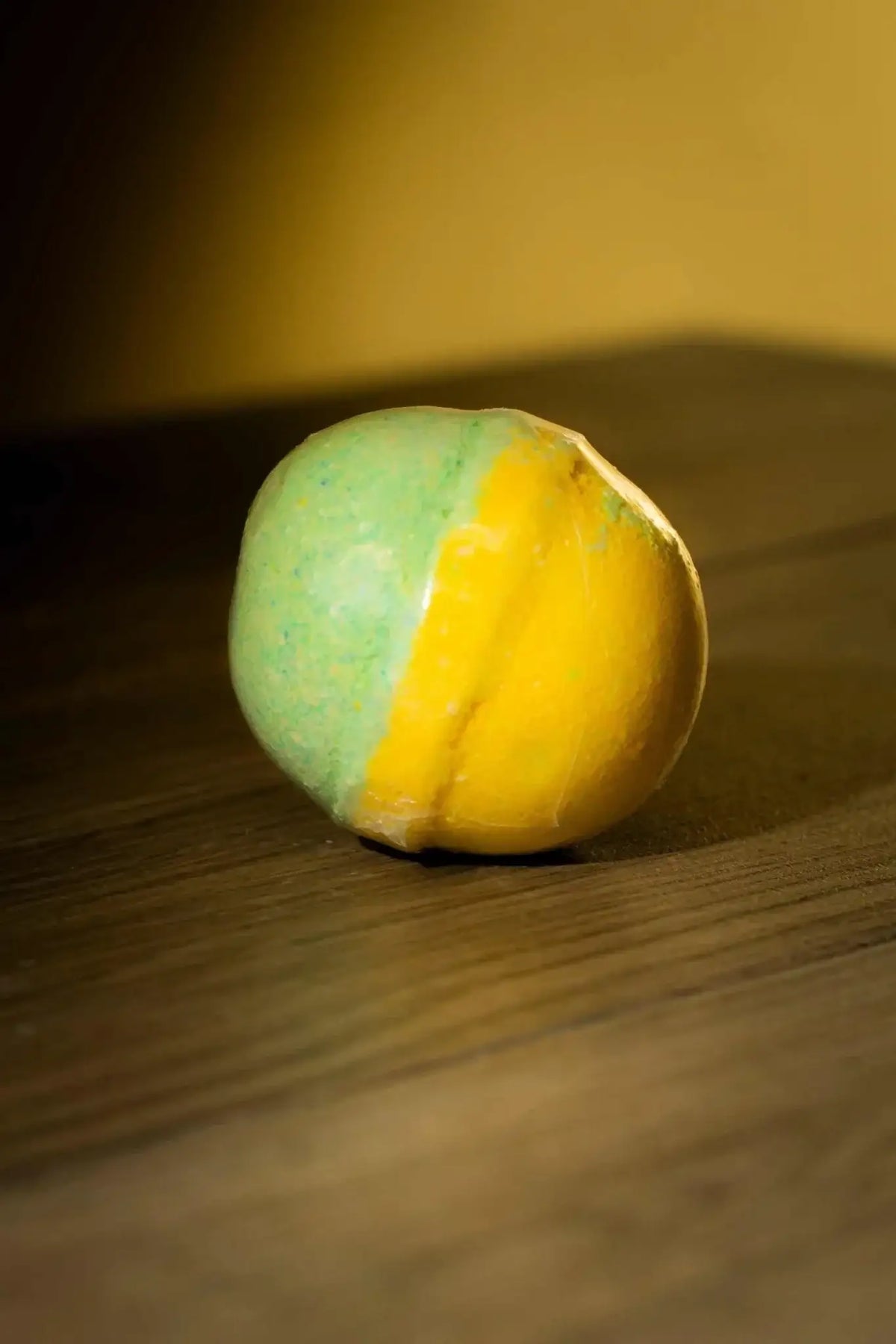 Luxurious Body Bath Bomb in vibrant yellow and green hues on a wooden surface.