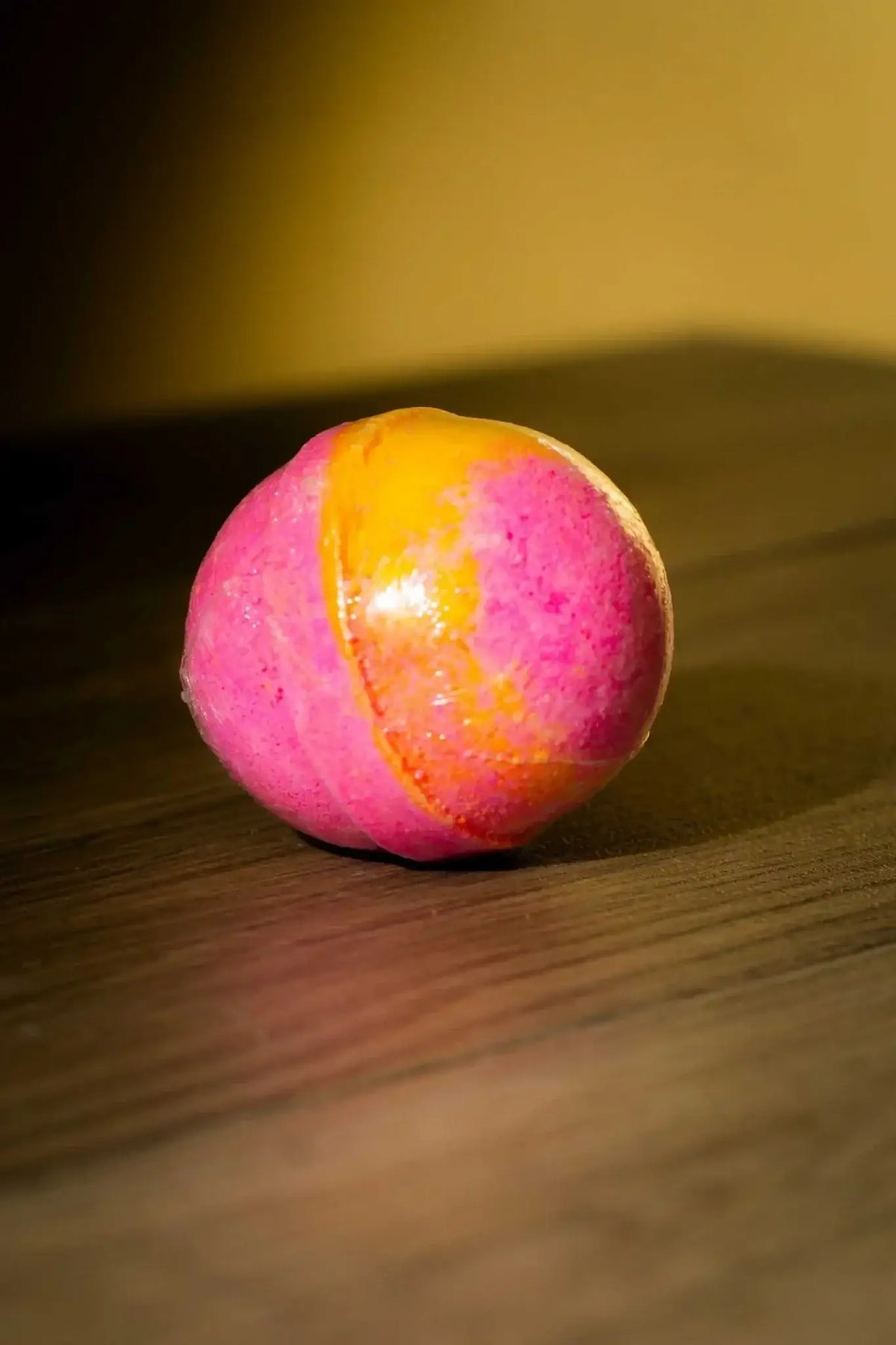 Luxurious Body Bath Bomb in vibrant pink and orange colors on a wooden surface.