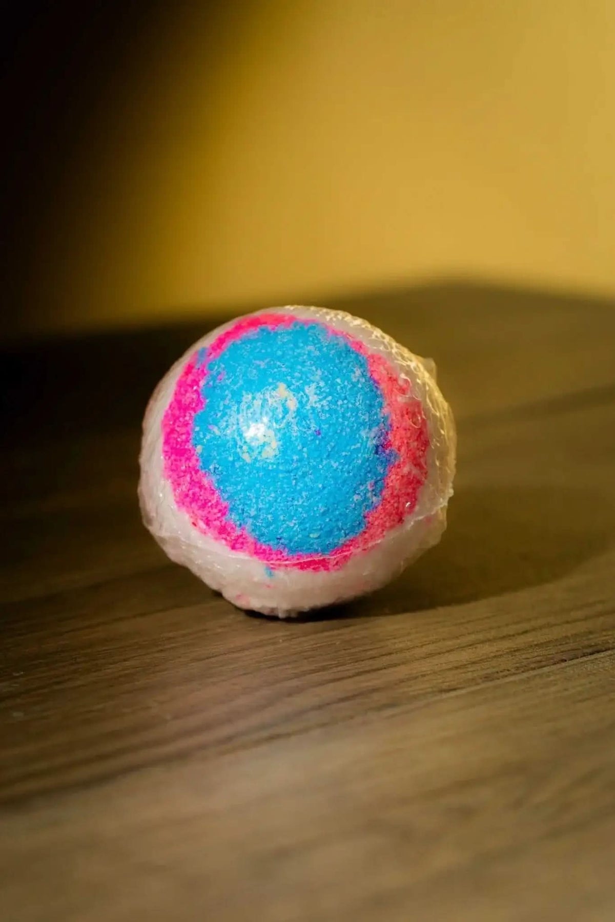 RoyalLuxsLLC luxurious herbal bath bomb with vibrant blue and pink colors on wooden surface