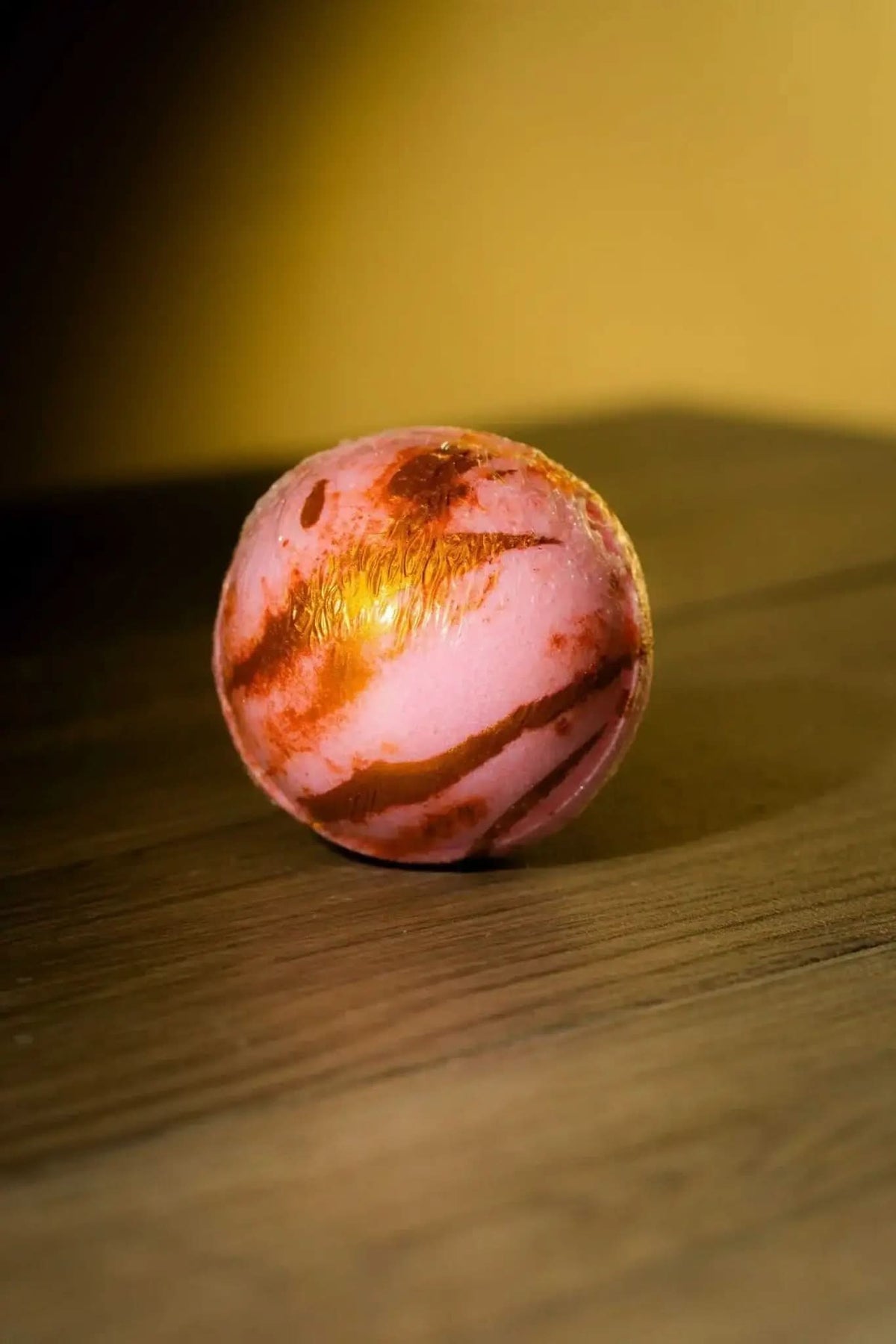 RoyalLuxsLLC luxurious herbal bath bomb in pink with gold and brown swirls on wooden surface