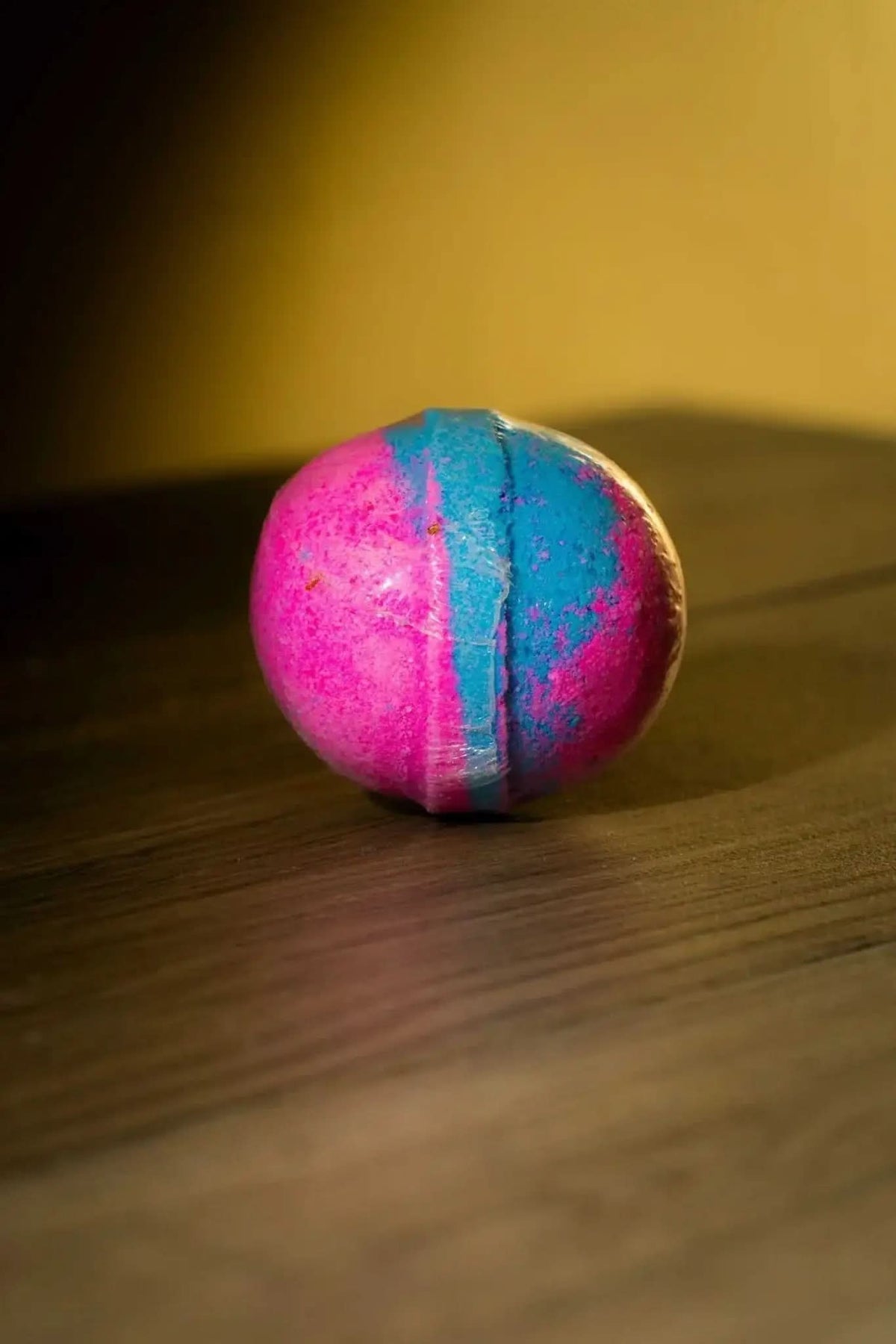 RoyalLuxsLLC luxurious herbal bath bomb in pink and blue resting on wooden surface