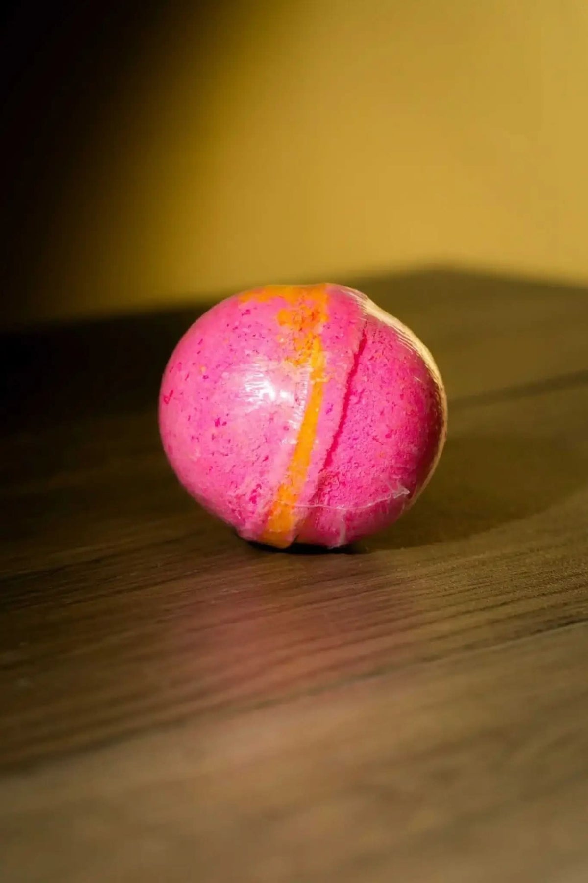 RoyalLuxsLLC luxurious herbal bath bomb in pink and orange resting on wooden surface