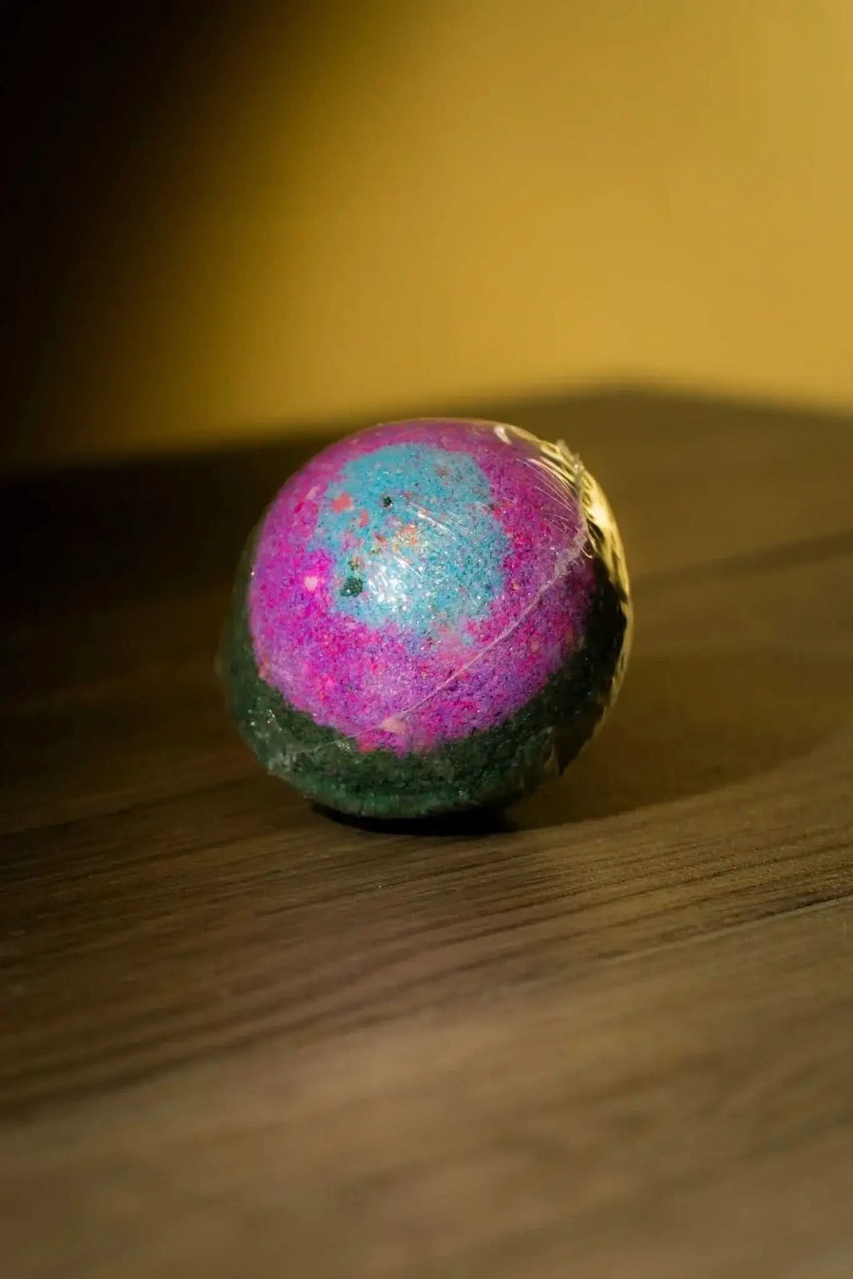 RoyalLuxsLLC luxurious herbal bath bomb in vibrant pink blue and green colors on wooden surface