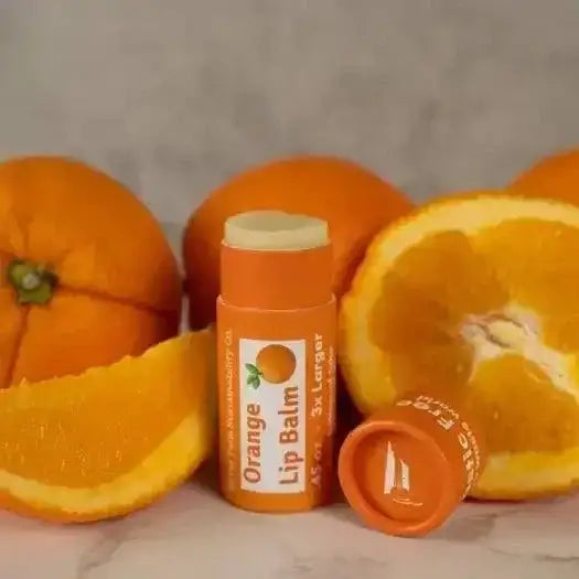 Natural Lip Balm next to fresh oranges, showcasing organic ingredients for soft, healthy lips, packed with herbal tonic benefits.