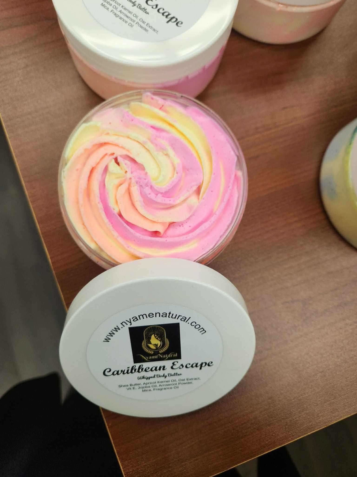 RoyalLuxsLLC Caribbean Escape body butter with swirled pink and yellow cream in a white jar on a wooden surface