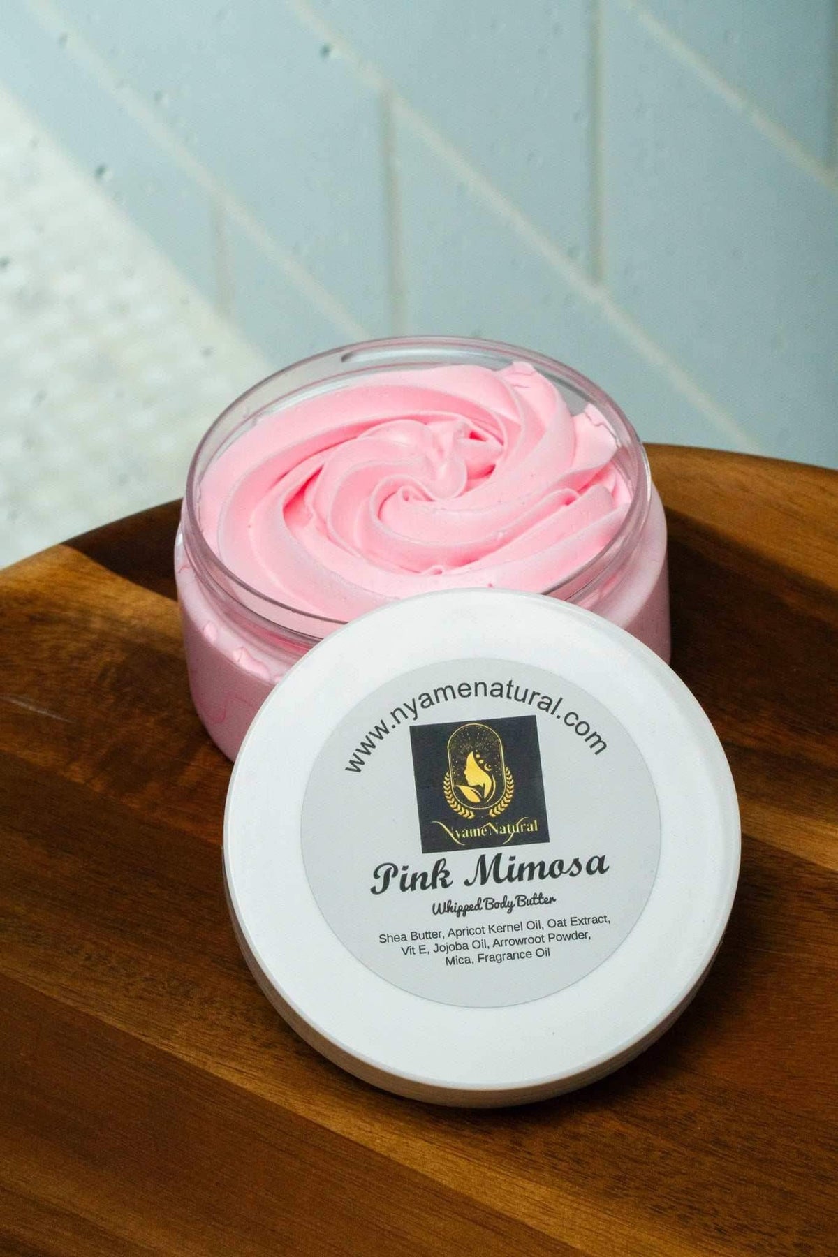 Pink Mimosa Body Butter in a jar on a wooden surface, showcasing its silky texture and hydrating properties.