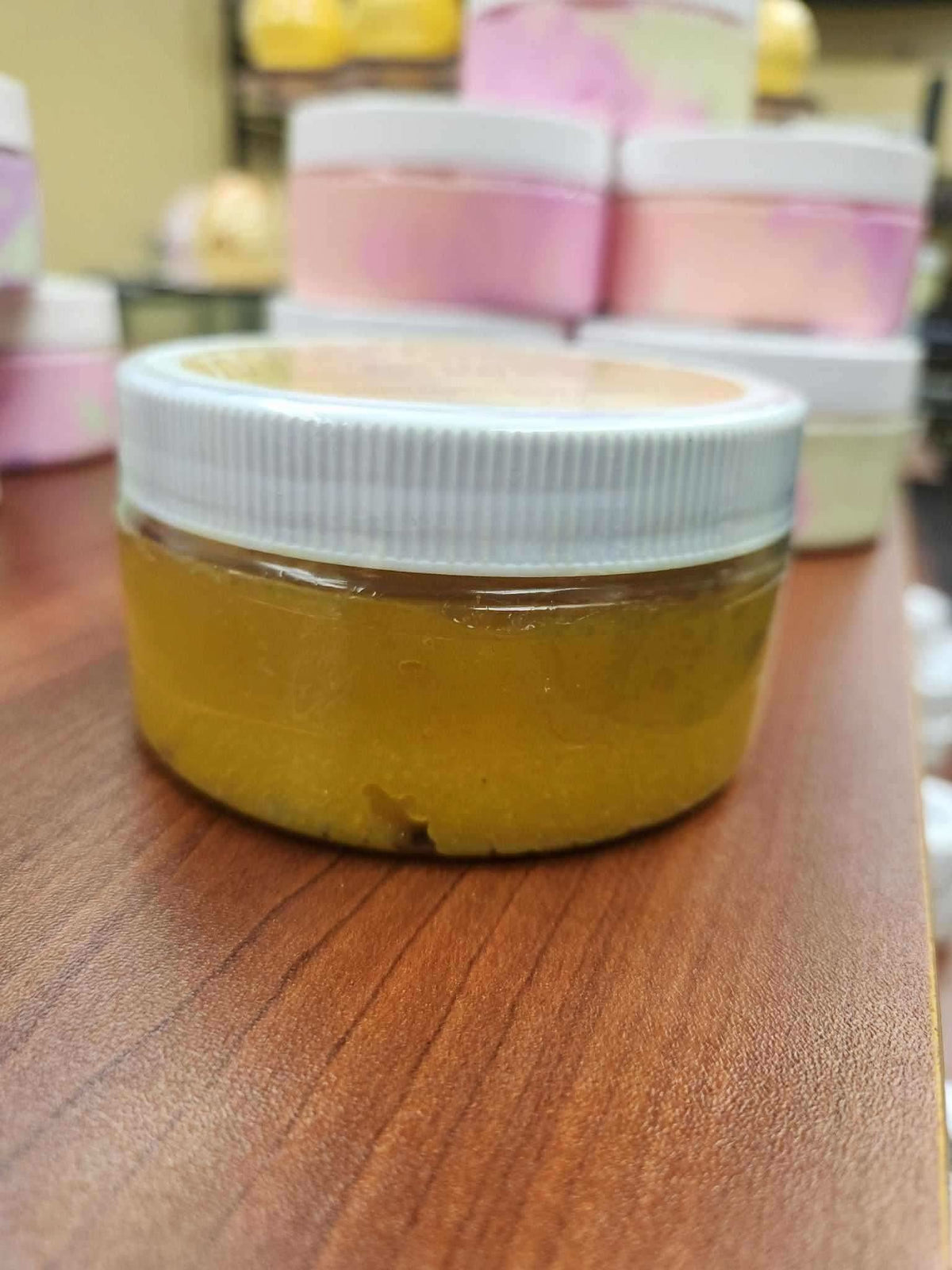 RoyalLuxsLLC turmeric papaya body scrub in a clear jar with white lid on wooden surface